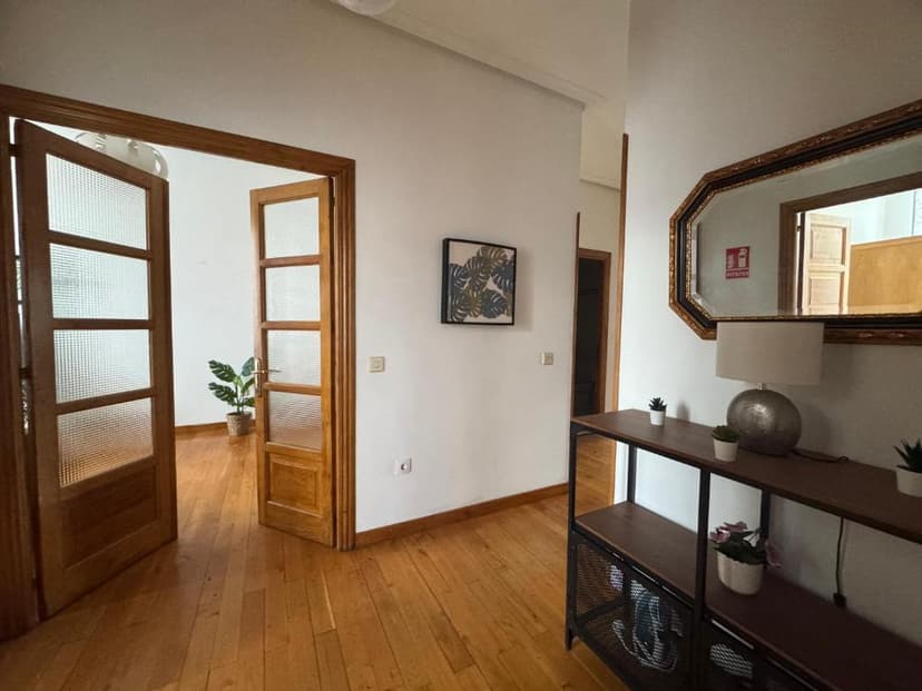Hallway interior with wood floors, open glass-paneled doors, and a console table with a mirror.
