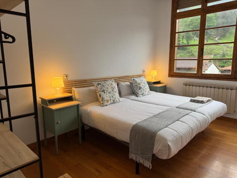 Twin beds with white linens in a room with wooden floors and a view of green hills.