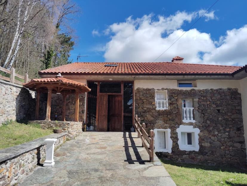 Stone and stucco building with wooden gazebo entrance under a blue sky with clouds.