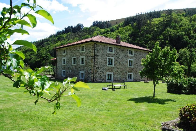 Stone rural apartment building with green lawn and forested hill in background