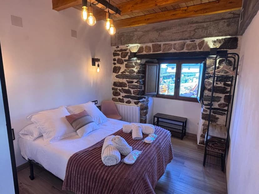 Cozy bedroom with white linens, stone accent wall, and exposed wooden beams in Casa Uría, Cam. Santiago.