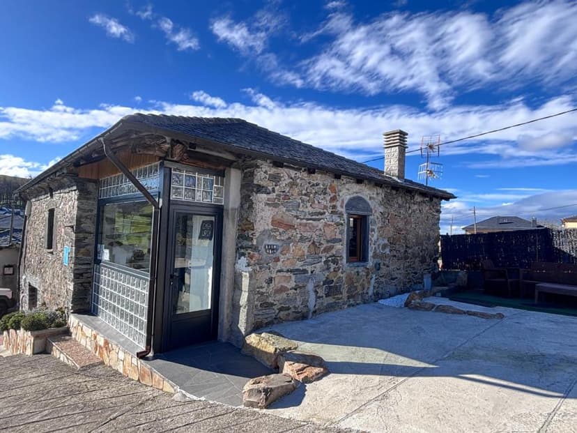 Stone house with slate roof and glass block windows, Casa Uría, under a blue sky.