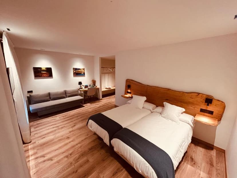 Hotel room with twin beds, wooden headboard, sofa, and desk area in A Reigada.