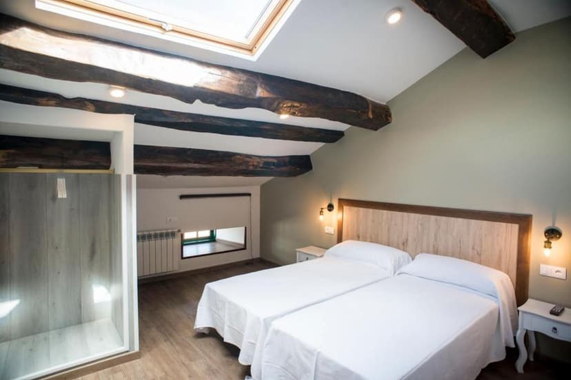Twin beds in attic hotel room with exposed dark wood beams and skylight