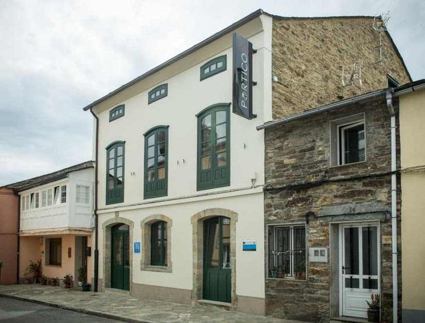 Hotel Portico building with white facade and green windows next to stone building on street
