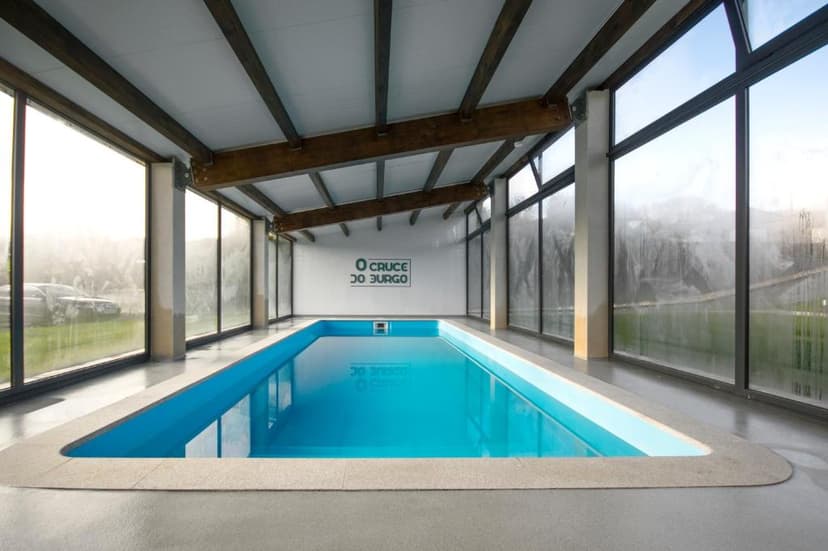Indoor swimming pool with bright blue water at Hotel Rural O Cruce do Burgo.