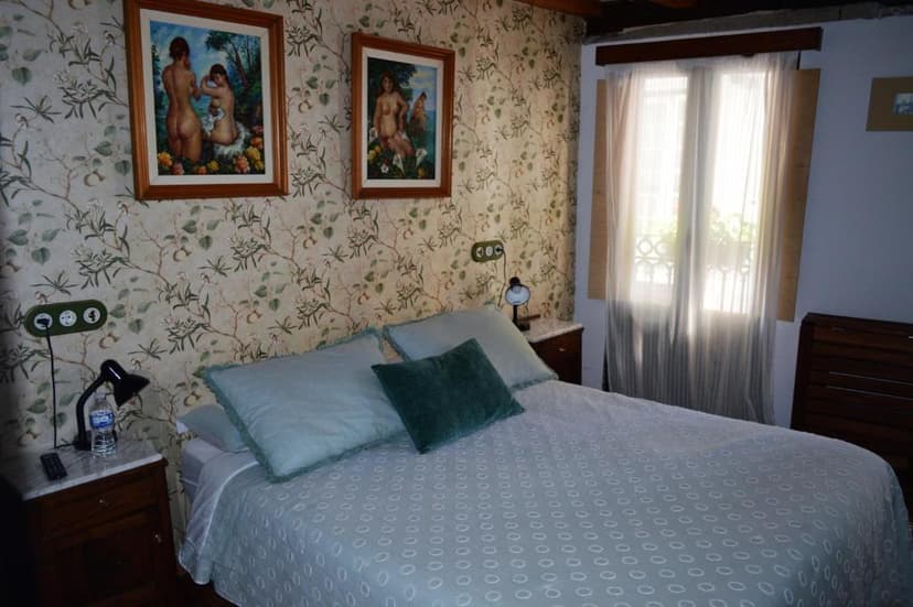 Bedroom with patterned wallpaper, two framed nude paintings, and a bed with light blue bedding.