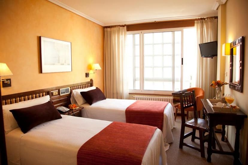 Twin hotel room with orange walls, white bedding, and a large window with sheer curtains.