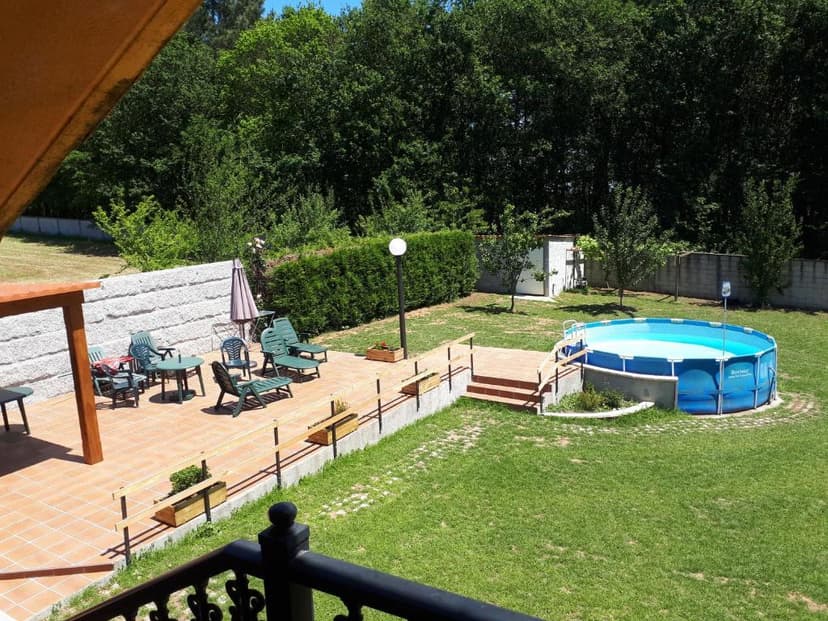 Patio with lounge chairs, umbrella, and above-ground pool in a grassy yard with trees.