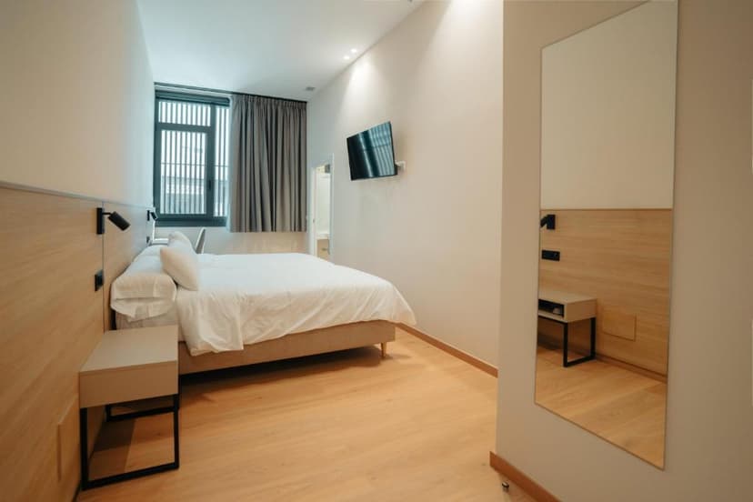 Modern hotel room with white bedding, light wood accents, and a large vertical mirror