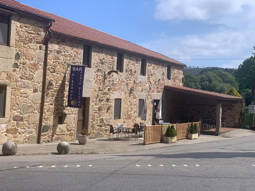 Stone albergue and bar with outdoor seating on a road in Ponte Olveira.