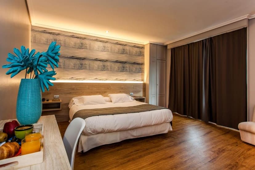 Hotel room with large bed, wooden floors, and turquoise vase with flowers, Hospedium Hotel La Marina.