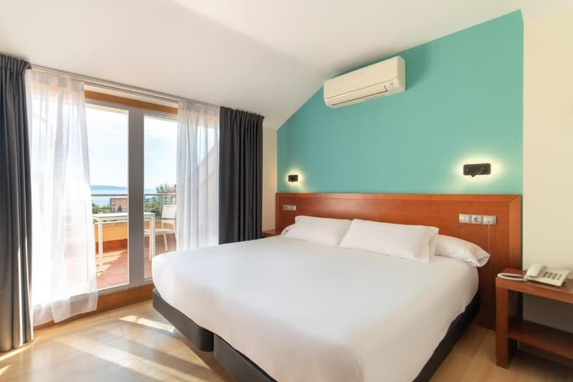 Hotel room with white bedding, wood headboard, and balcony view of the sea in Hotel Playa Langosteira.