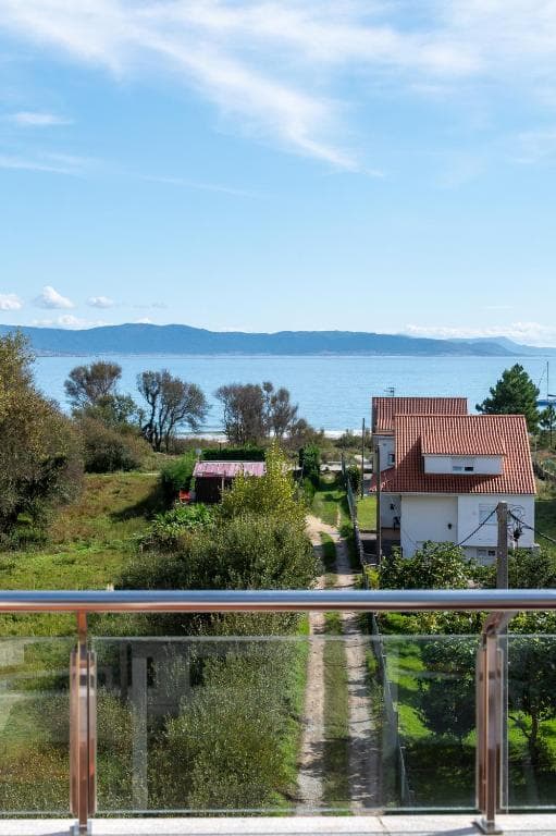 View from balcony over greenery to houses, beach, and mountains across the sea at Hotel Playa Langosteira.