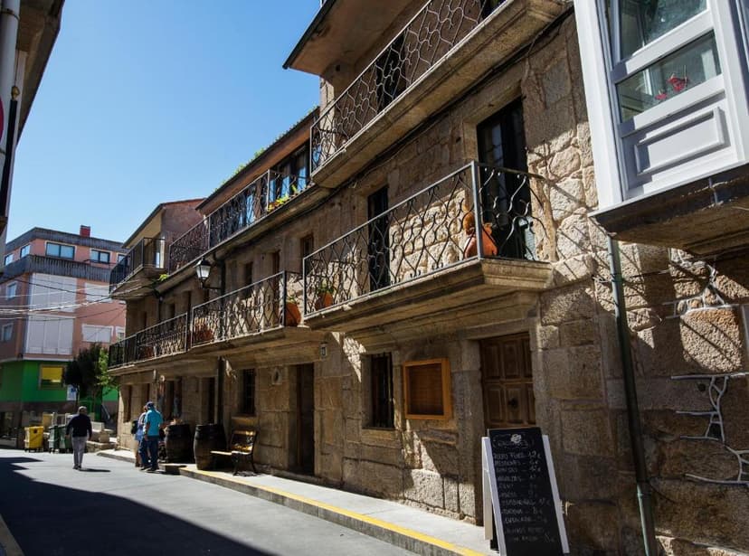 Stone building with wrought iron balconies on a sunny street in a rustic German pension setting.