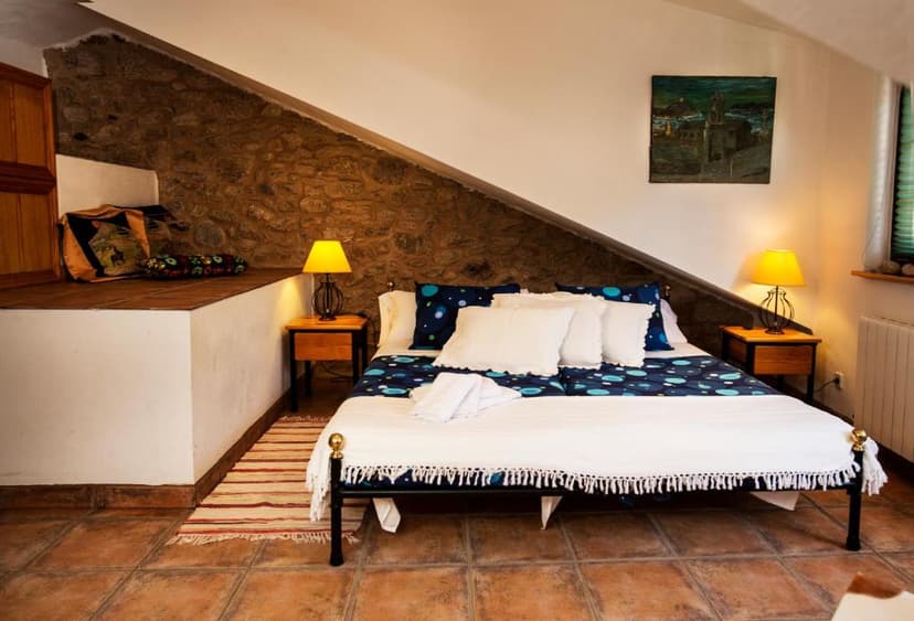 Rustic bedroom with stone wall, white bedding, and yellow lamps in an attic space