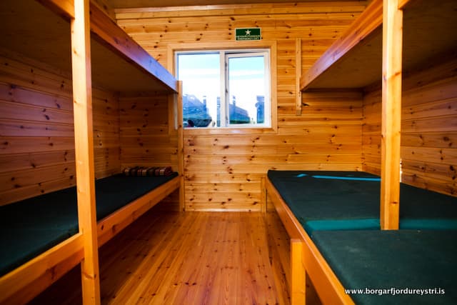 Wooden bunk room interior with green mattresses, viewed from the center aisle, Húsavíkurskáli.