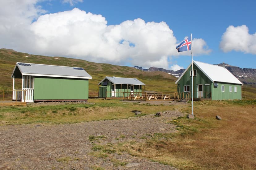 Green cabins with solar panels and an Icelandic flag near mountains in Loðmundarfjörður.