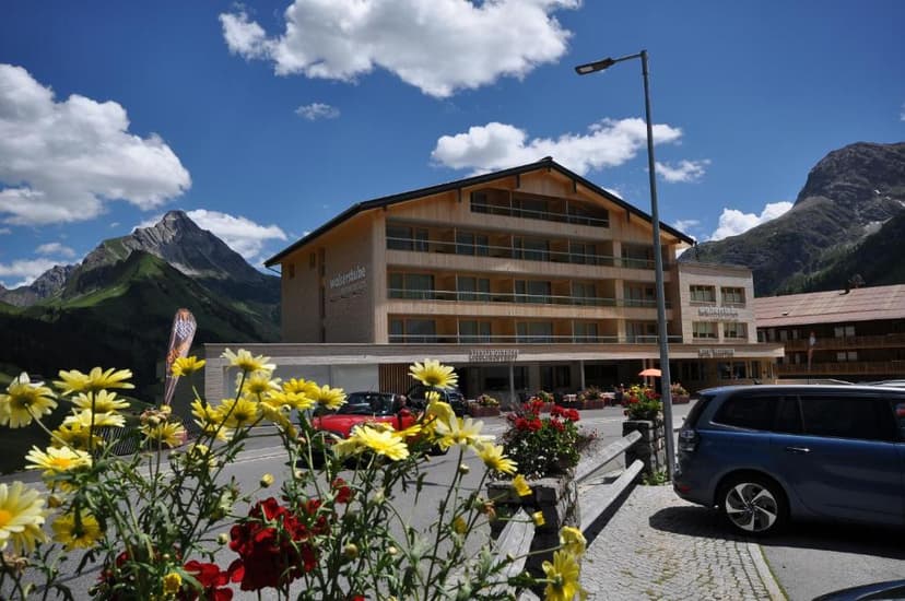 Hotel Walserstube building with wooden facade against green mountains under blue sky with clouds.