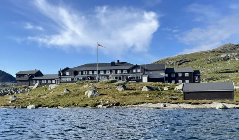 Finsehytta lodge by lake shore with Norwegian flag flying under blue sky.
