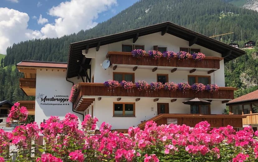 Landhaus Moosbrugger pension with flower boxes in front of a steep, forested mountain.