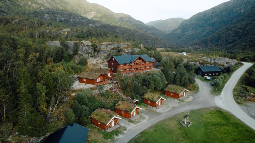 Wooden cabins with grass roofs and a lodge nestled in a steep, forested mountain valley, likely Østerbø Fjellstove.