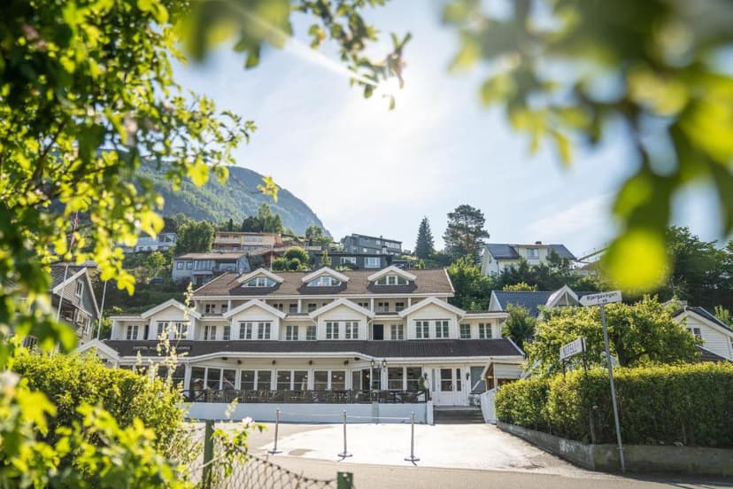 Aurland Fjordhotell building nestled on a steep hillside under bright sun, framed by foliage.
