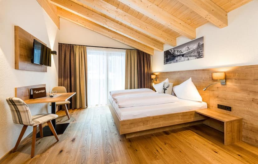 Hotel room with wood accents, platform bed, desk, and balcony view at Landhaus Moosbrugger