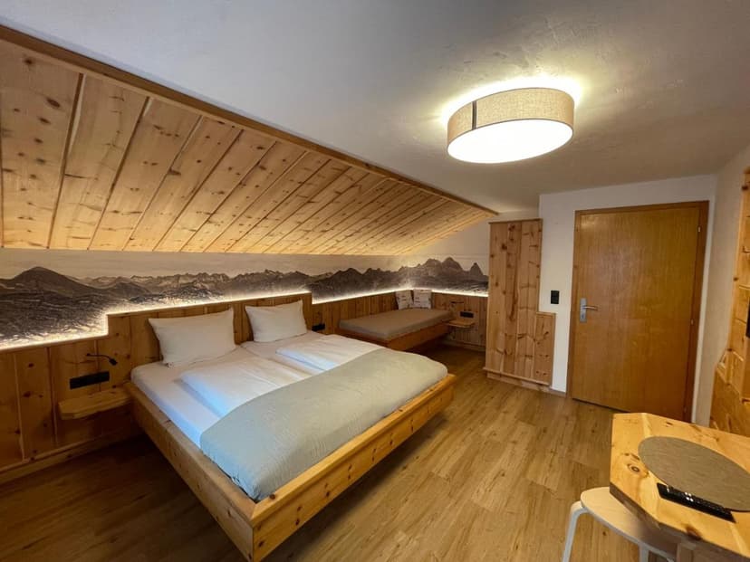 Wood-paneled hotel room with large bed, mountain mural, and sloped ceiling, Haus Walch.