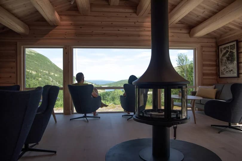 Lounge with modern fireplace and view of green mountains and lake at DNT Bjørnhollia.