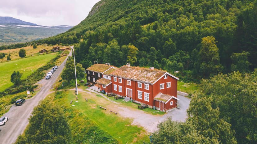 Red wooden guesthouse with grass roof nestled in green mountainside near Gjevillvasshytta.