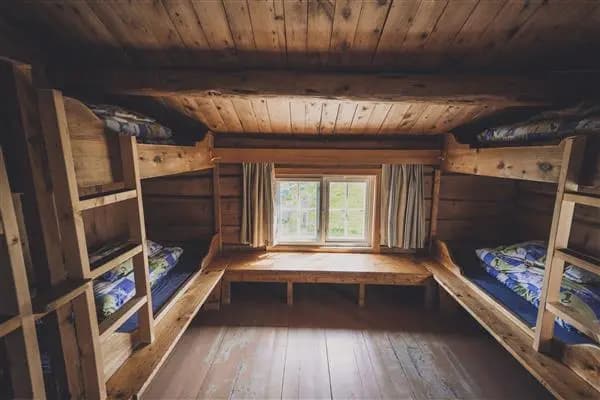 Wooden bunk room interior at Jøldalshytta with window view of greenery.