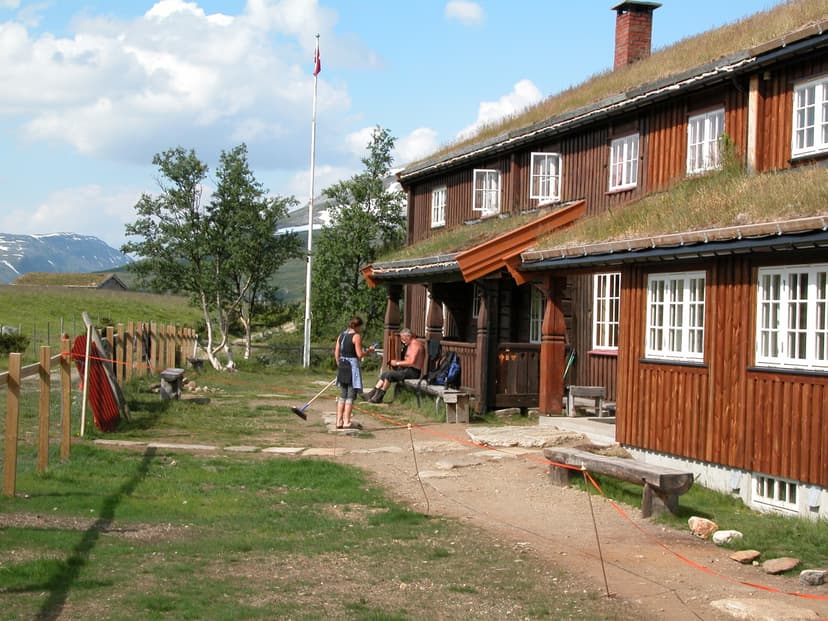 Jøldalshytta mountain lodge with grass roof, people outside, and snow-capped mountains.