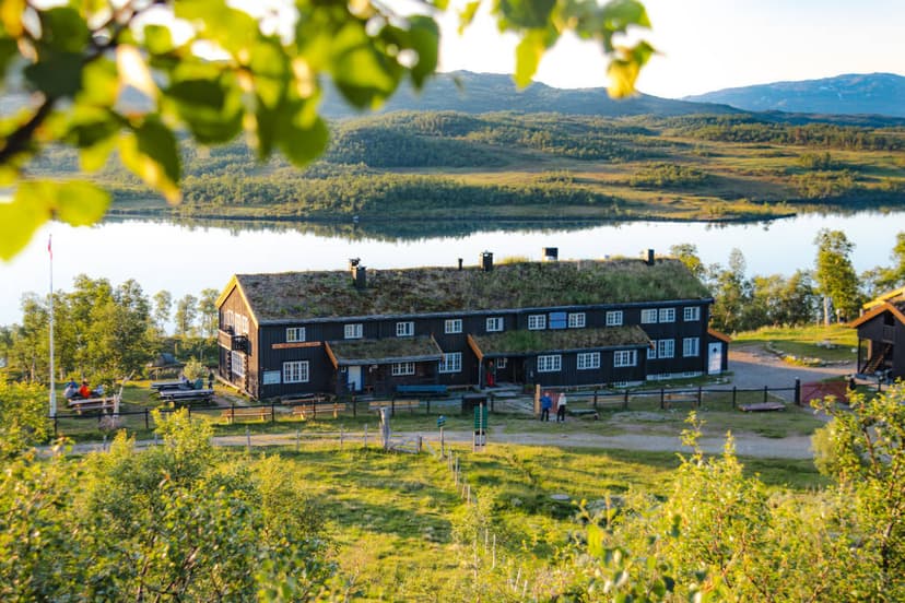 Jøldalshytta cabin with grass roof by lake, set against forested mountains.
