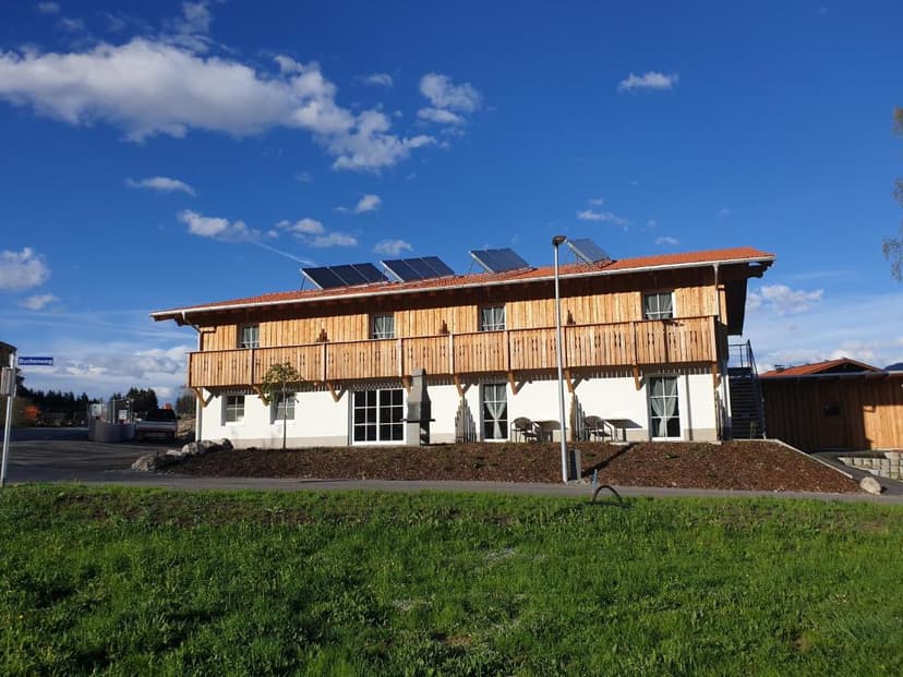Gästehaus am Hahnenkamm with wood balconies and solar panels under blue sky.