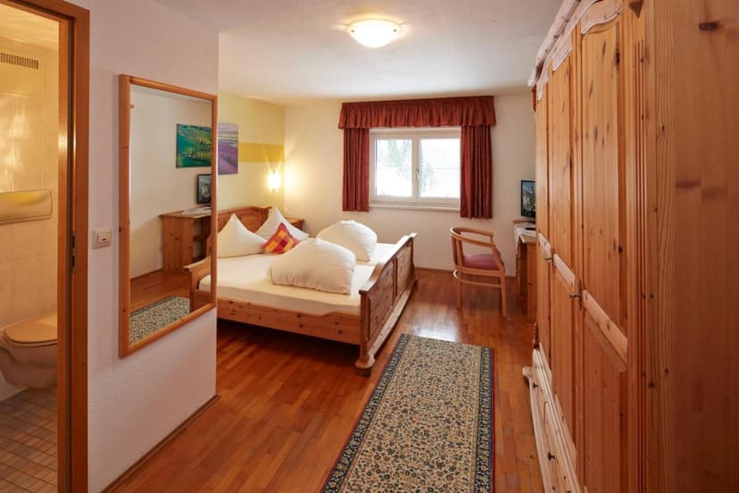 Alpenmotel Säuling guest room with wooden bed, wardrobe, and view into the bathroom.