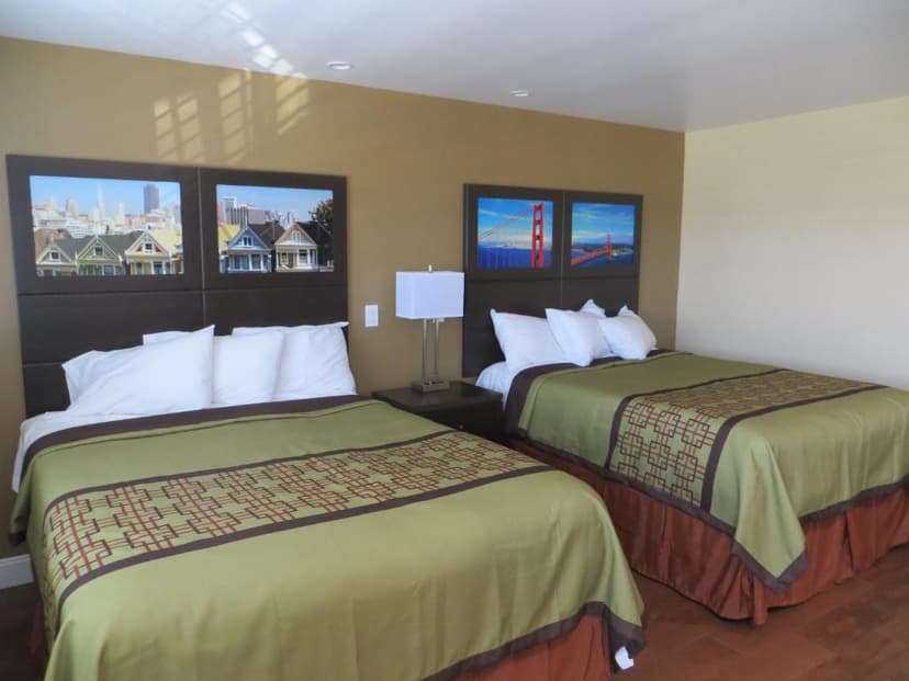 Two double beds in a hotel room with San Francisco landmark art above the headboards.