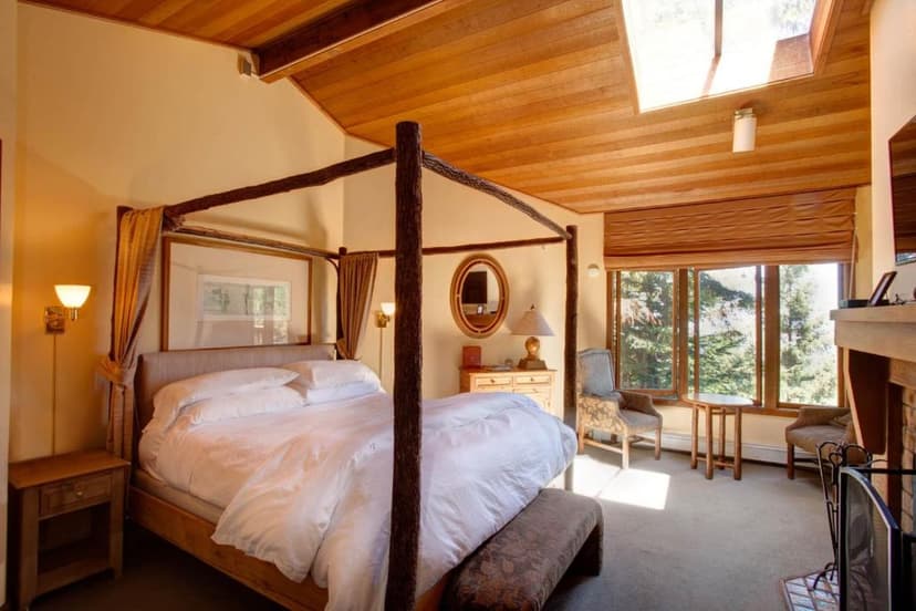 Bedroom with log canopy bed, wood ceiling, and large window view of pine trees.