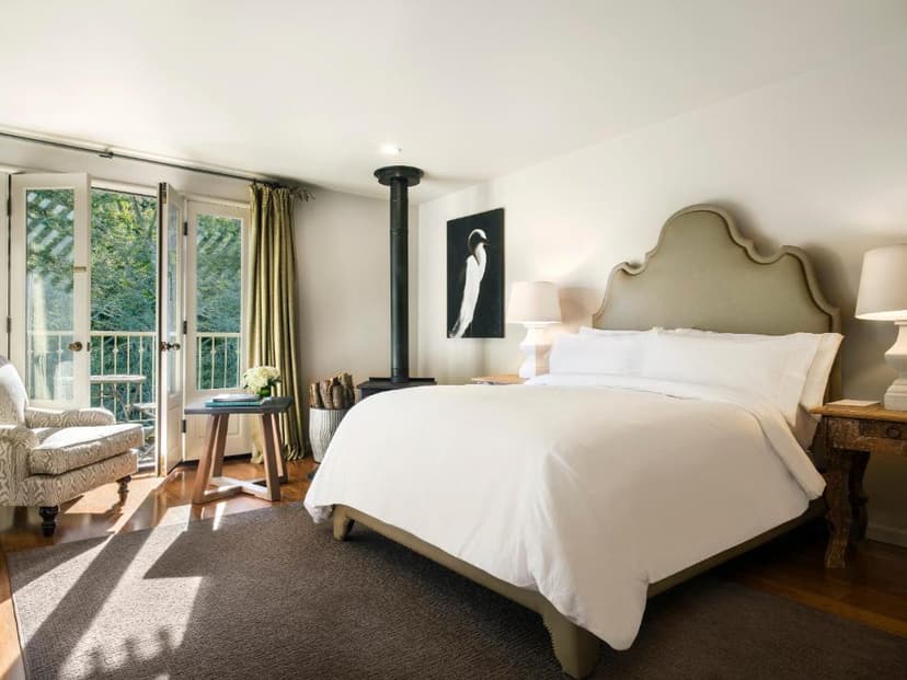 Bedroom with white bedding, wood stove, and balcony doors opening to greenery, Mill Valley Inn.