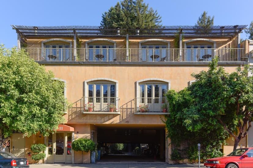 Mill Valley Inn building exterior with balconies, stucco facade, and lush green trees.