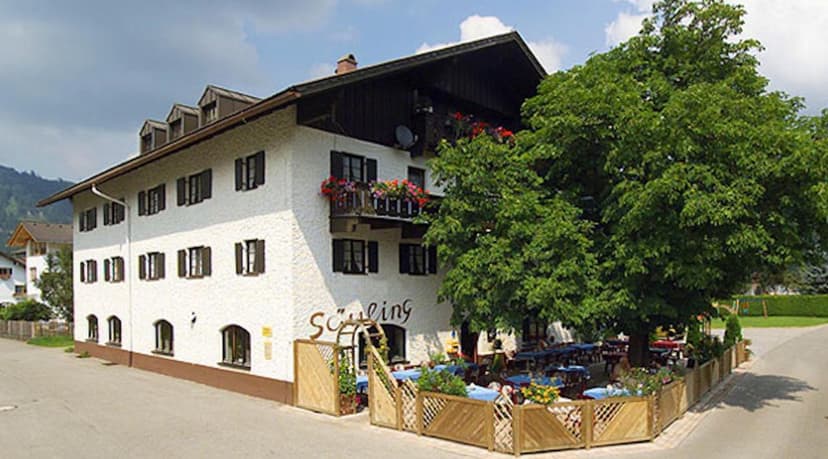 Alpenmotel Säuling building with outdoor dining patio and large green tree in summer.