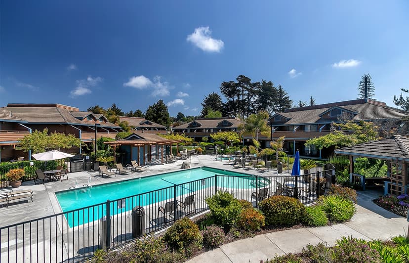 Swimming pool area with lounge chairs surrounded by brown-roofed buildings at Seacliff Inn Aptos.