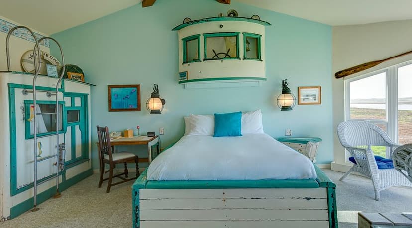 Nautical themed bedroom with white and teal bed, ship's wheel decor, and view of Moss Landing.