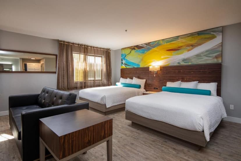 Hotel room with two queen beds, modern artwork, and a black leather sofa.