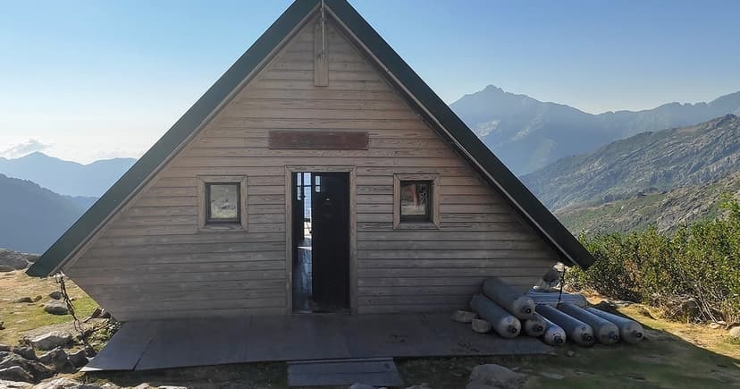 Refuge de Pietra Piana wooden hut with mountain backdrop and gas cylinders outside