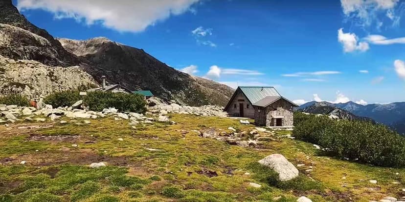 Refuge de Pietra Piana mountain huts on grassy slope under blue sky with distant peaks.