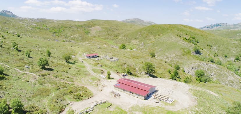 Mountain refuge with red roof nestled in rolling green hills under a blue sky, Bergerie I Croci.