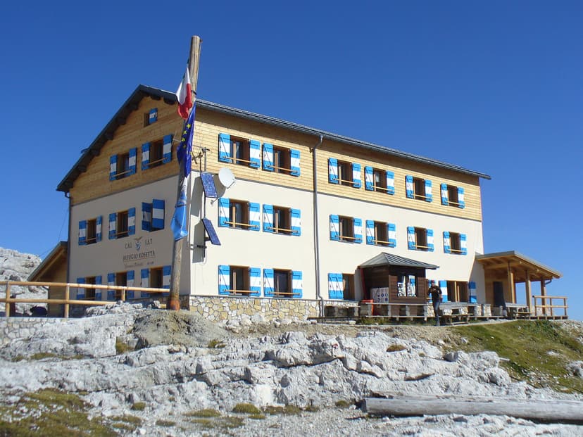 Rifugio Rosetta mountain hut with blue shutters under a clear blue sky on rocky terrain.