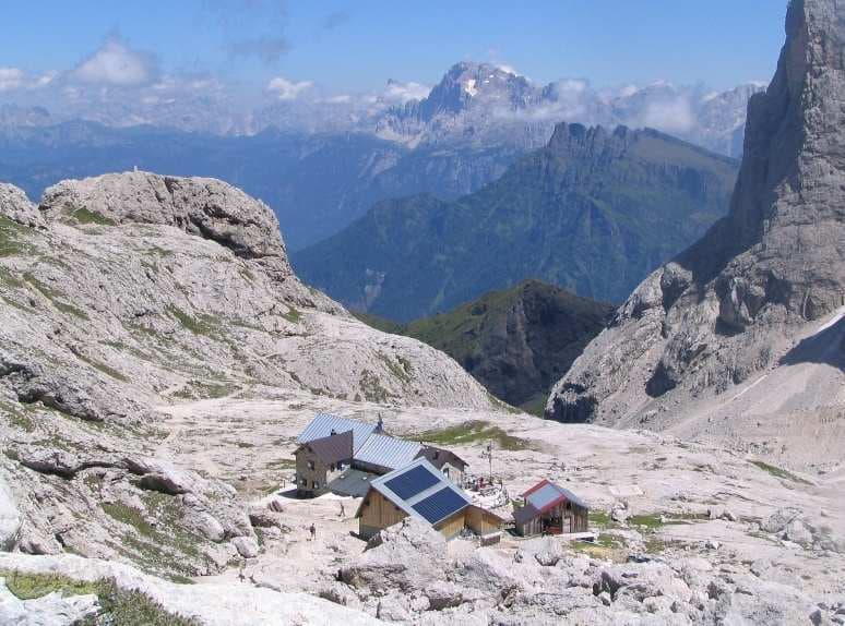 Rifugio Volpi al Mulaz mountain hut nestled among rocky terrain with distant Dolomite peaks.