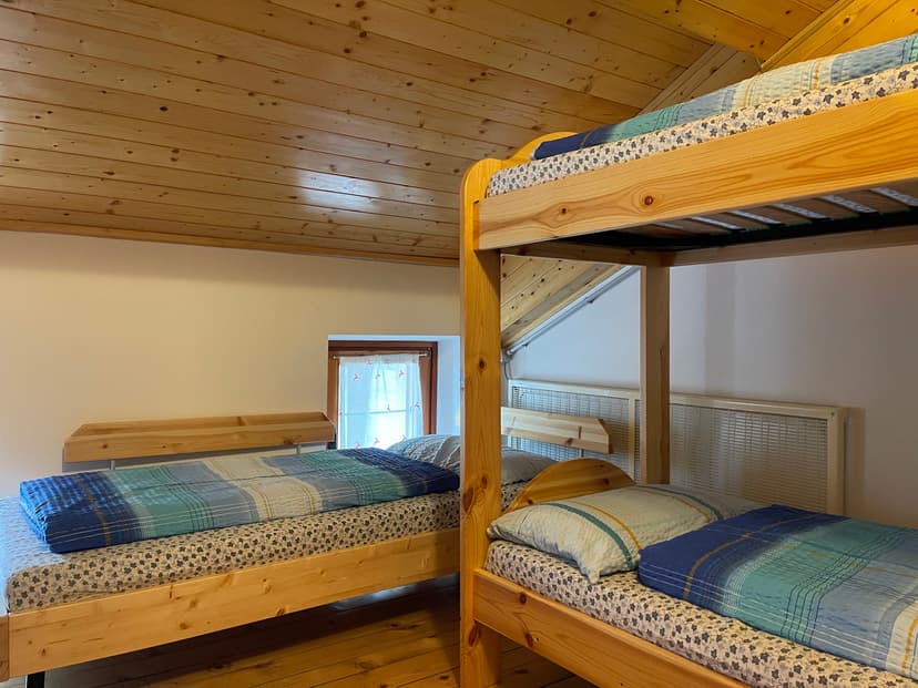 Bunk beds and single bed with wooden frames and blue bedding inside an attic room with wood paneling.